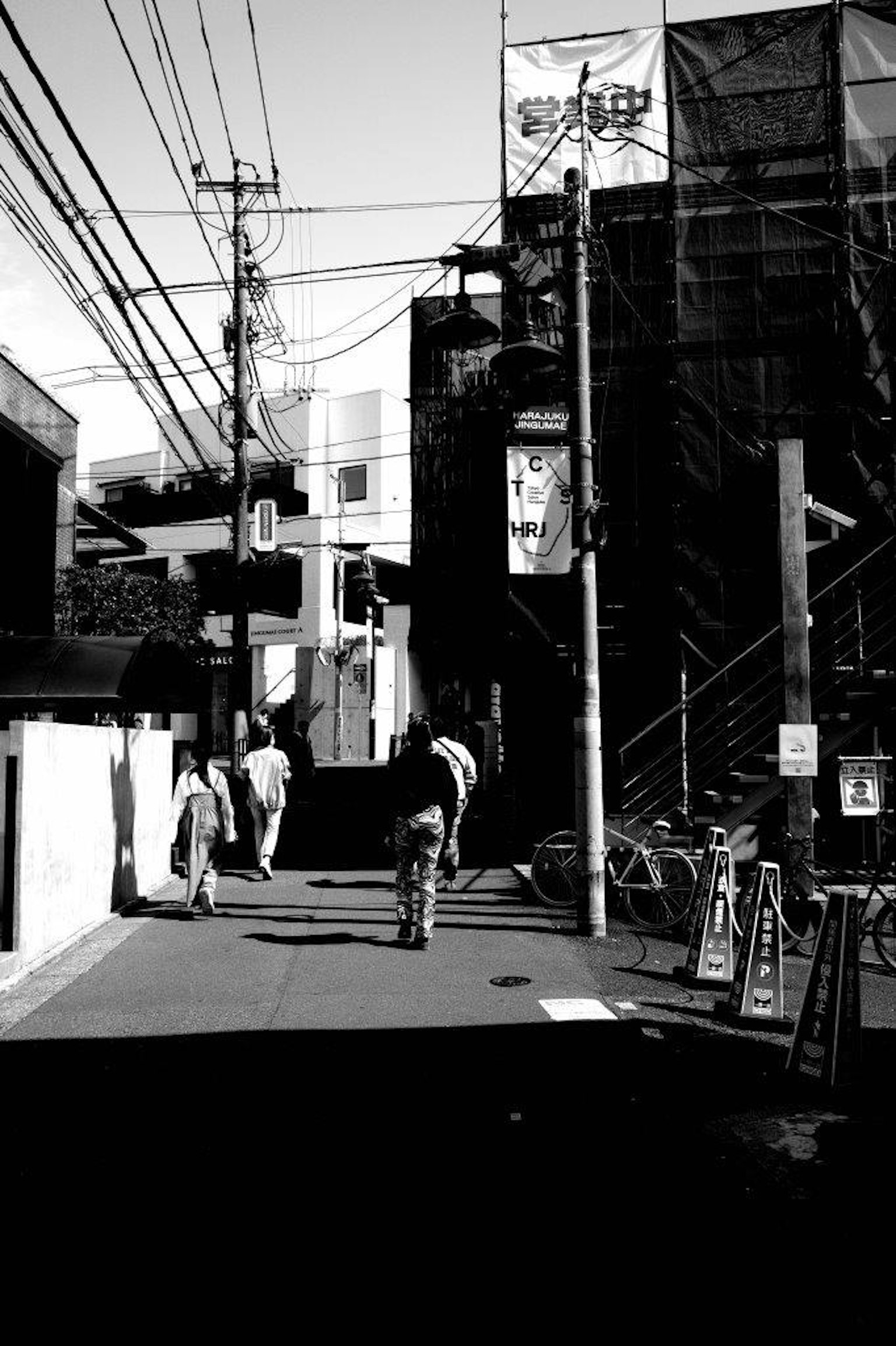 Black and white urban scene featuring a cyclist and pedestrians buildings and power lines visible