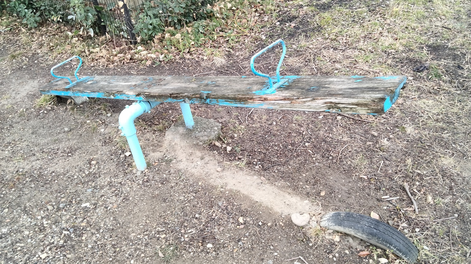 Alter Holzschaukel mit blauen Metallstützen in einem Park