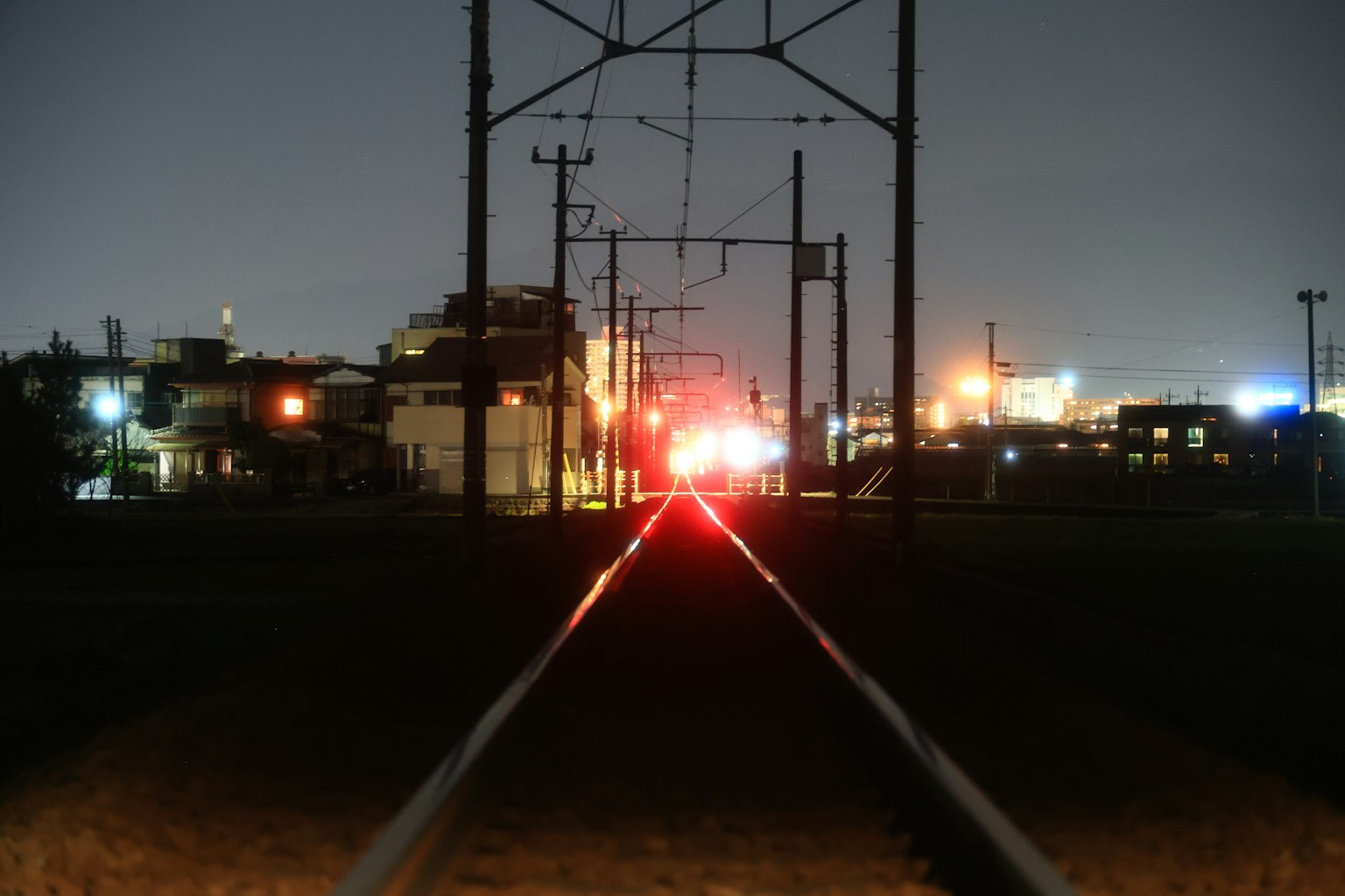 Vista notturna dei binari ferroviari con luci della città sullo sfondo