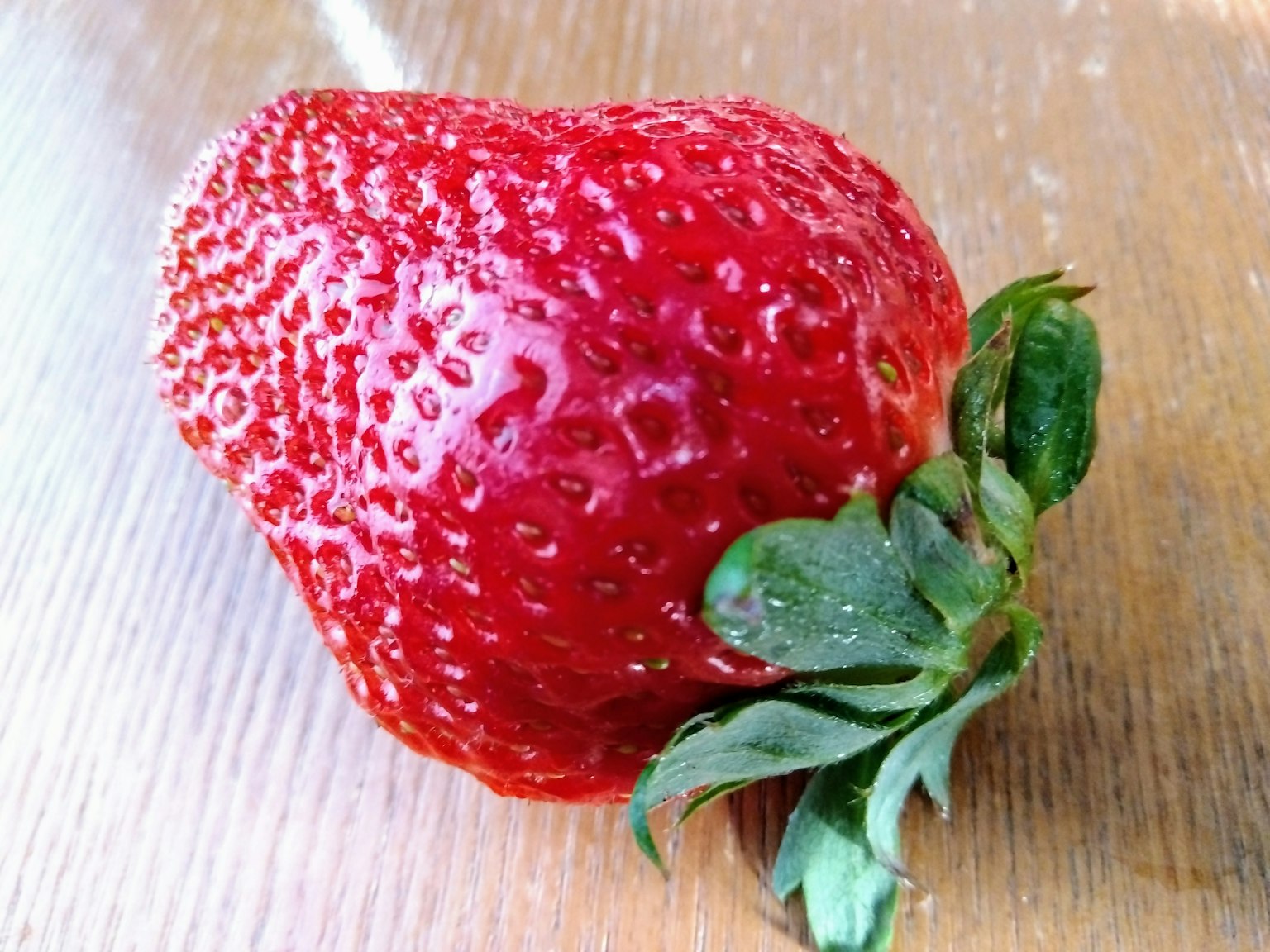 A fresh strawberry placed on a wooden table