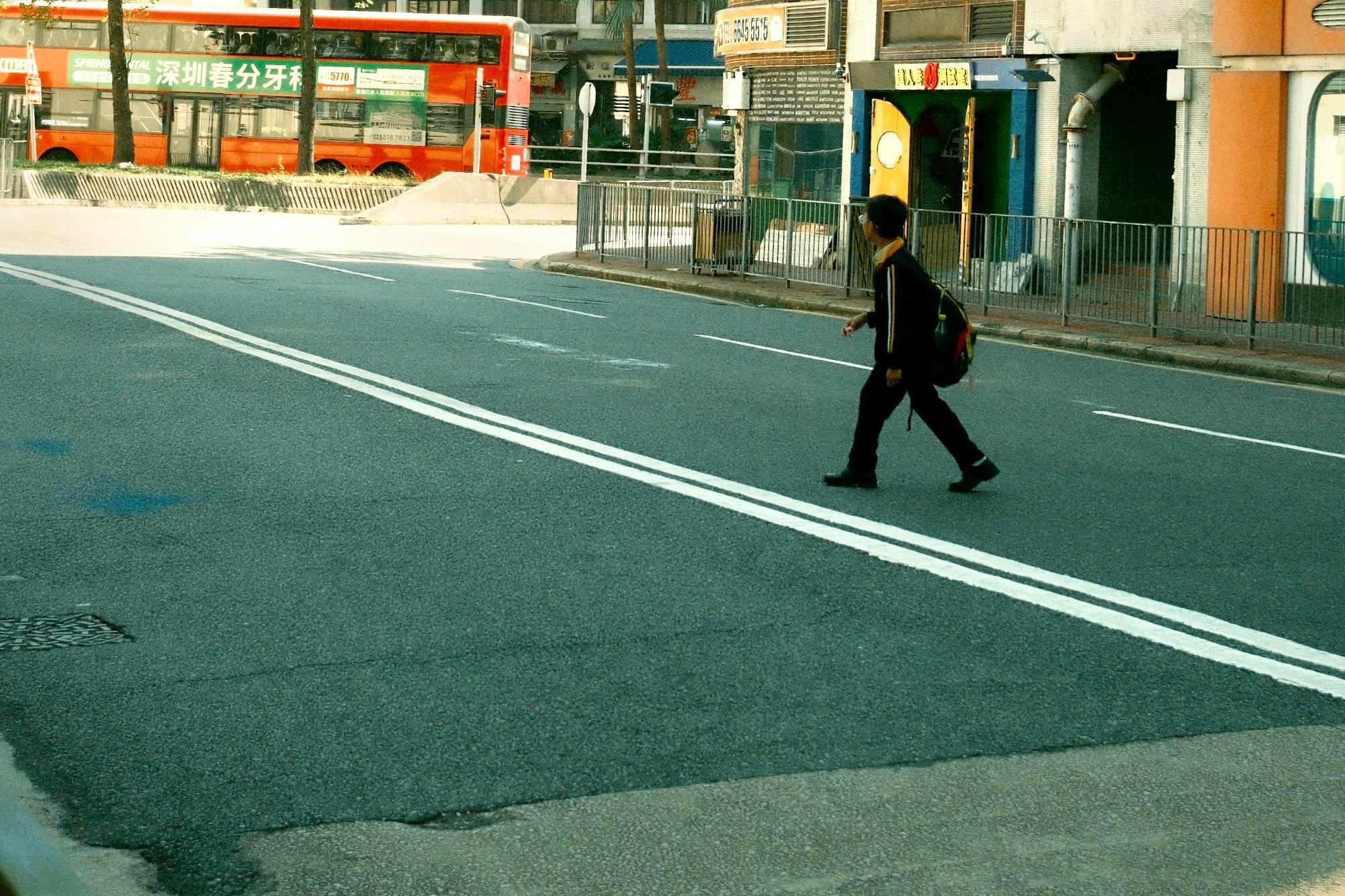 赤いバスが見える街角で歩く男性