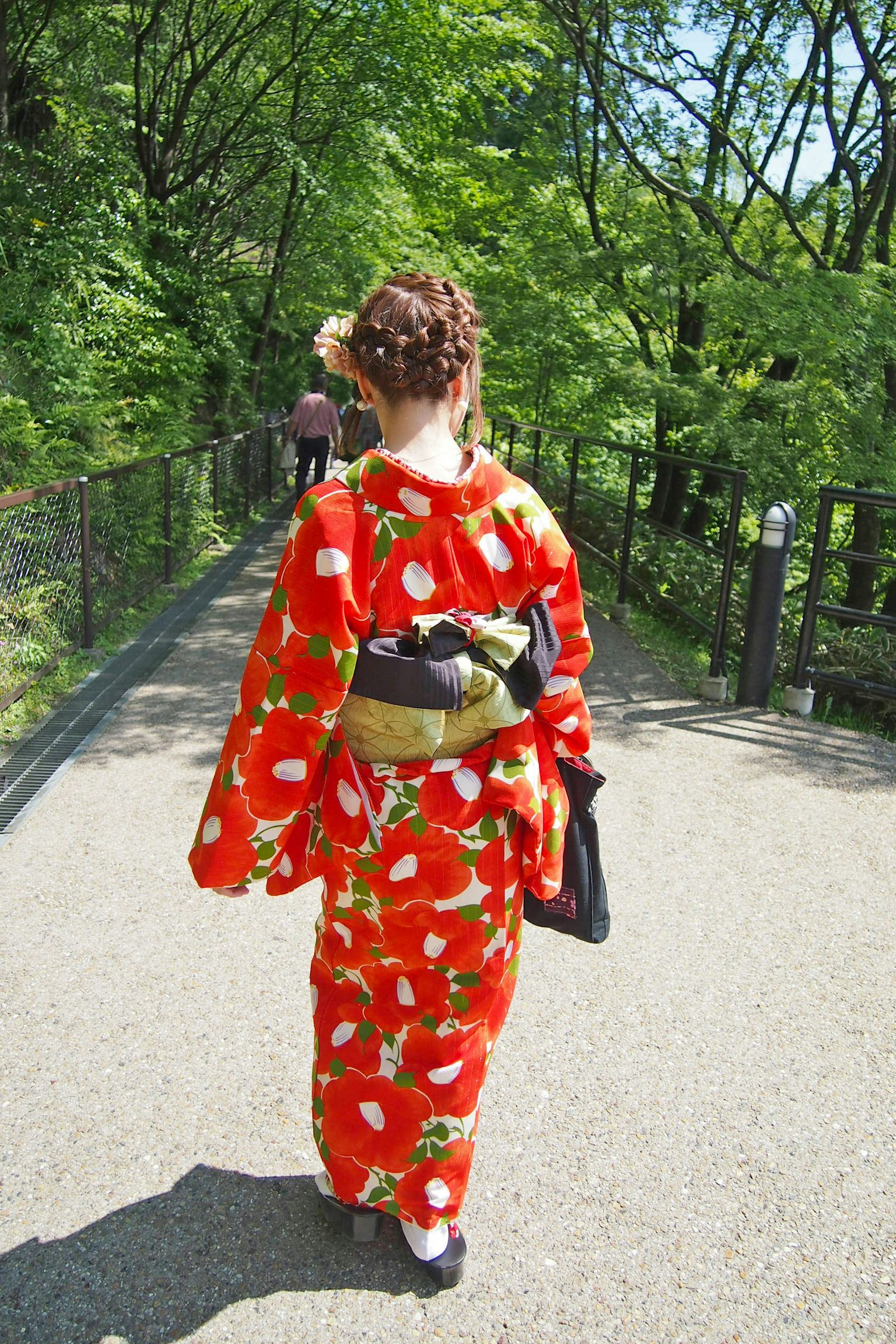Eine Frau im roten Blumenkimono, die durch grüne Bäume geht
