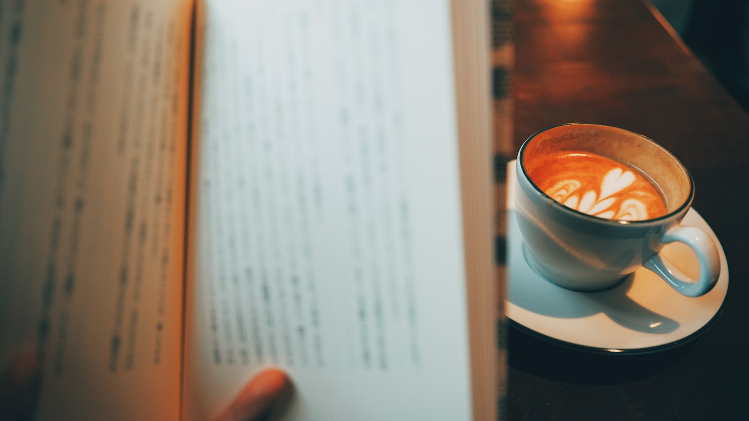 Una scena accogliente con una mano che tiene un libro e una tazza di caffè in primo piano