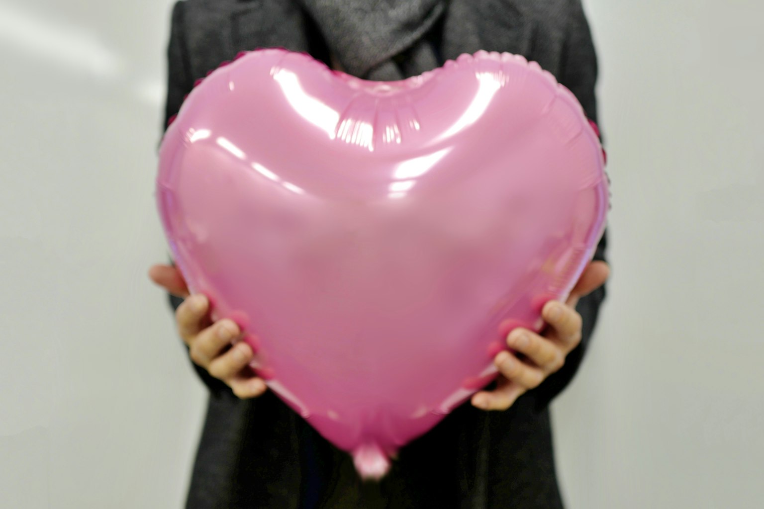 Orang memegang balon berbentuk hati besar berwarna pink