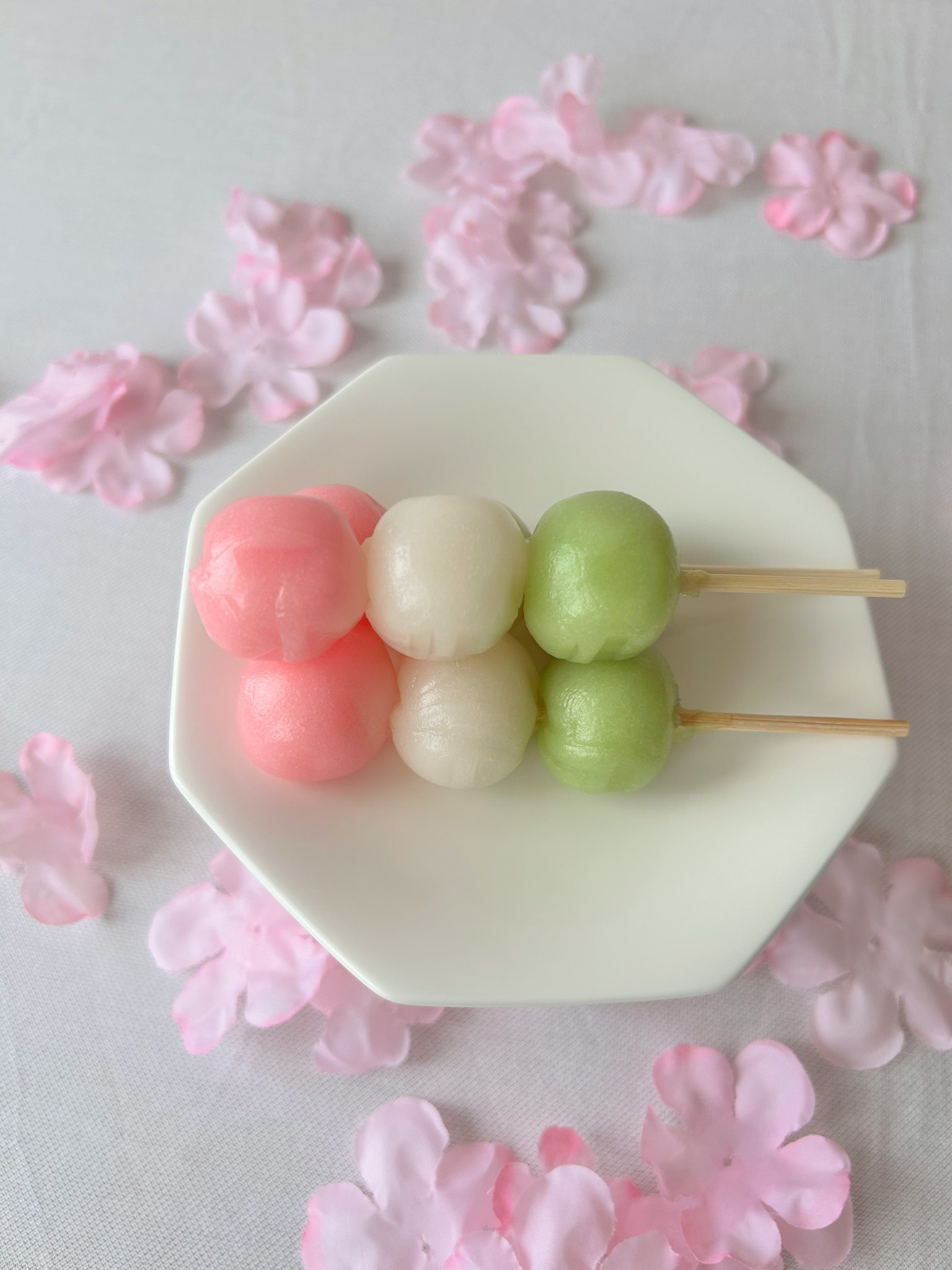 Xiên dango nhiều màu sắc được sắp xếp trên đĩa trắng với cánh hoa hồng