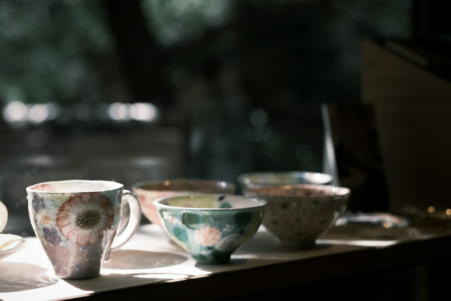 Cốc và bát gốm thủ công được sắp xếp trên bàn với ánh sáng tự nhiên