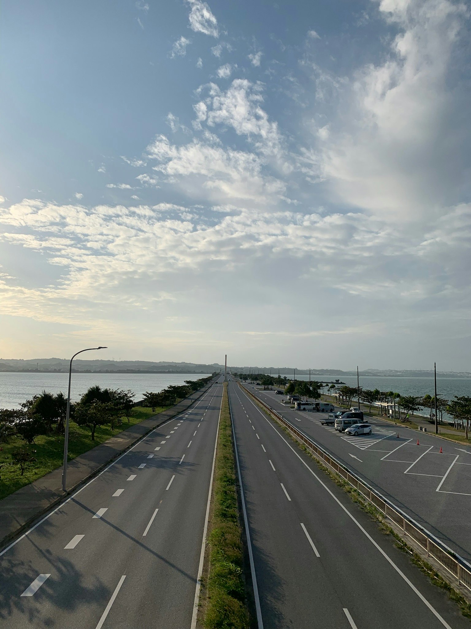 Amplia carretera junto al mar con cielo azul claro y nubes
