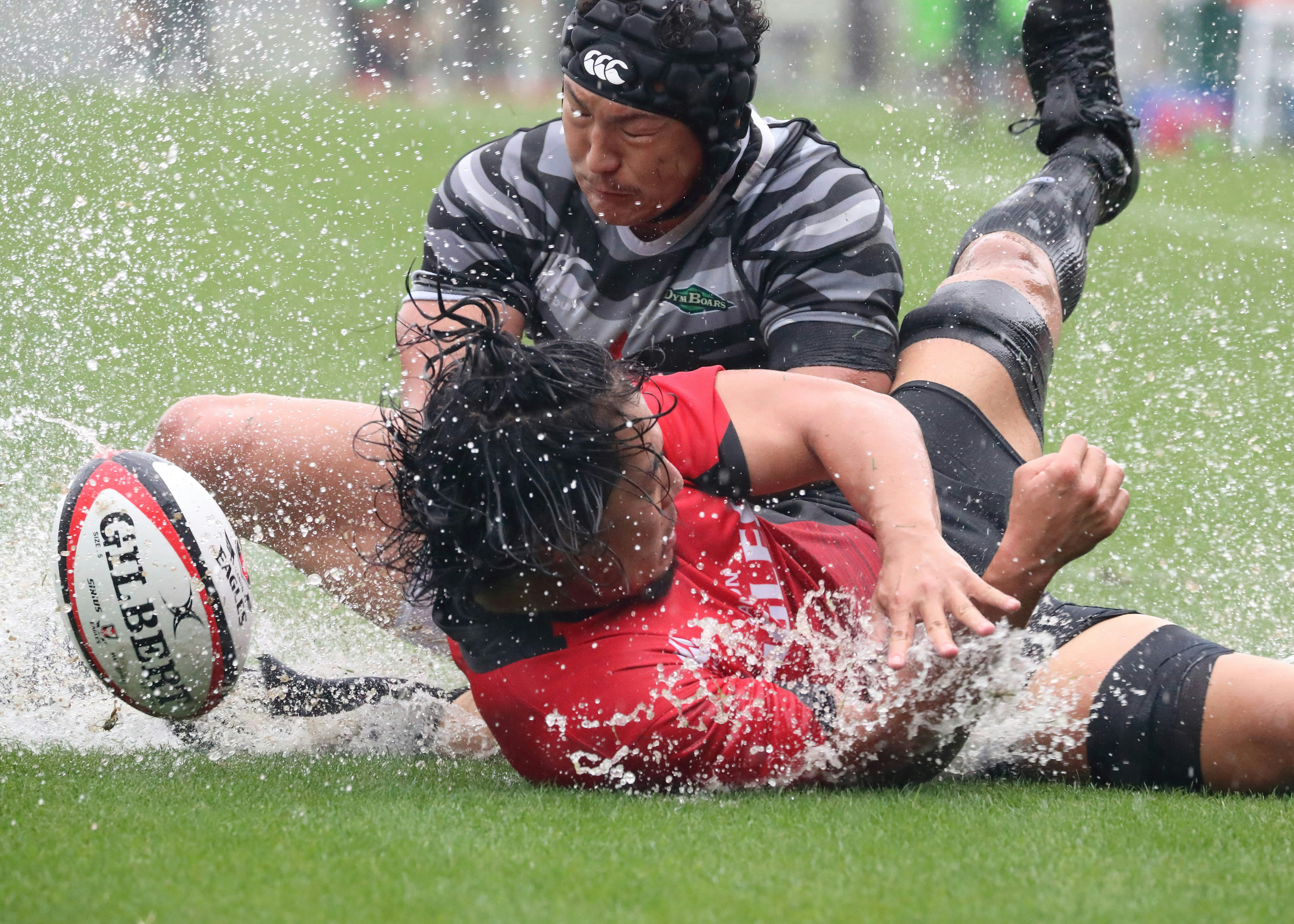 Rugby-Tackle im Regen mit Spielern auf nassem Gras