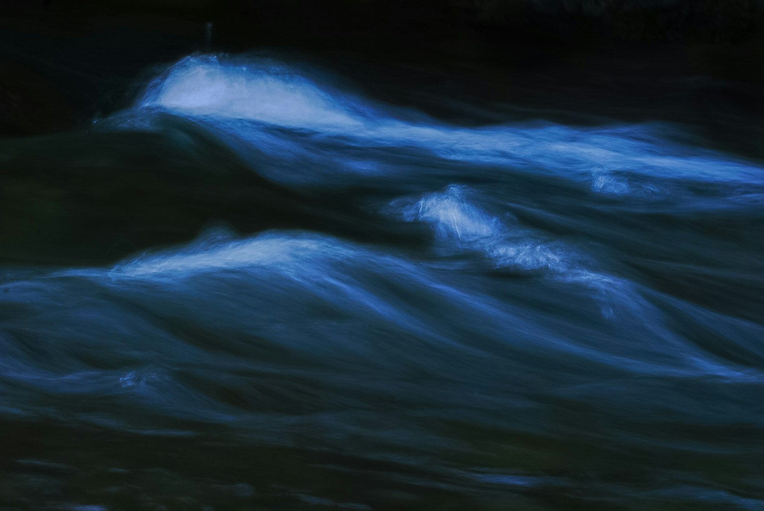Image of gentle blue waves flowing on a dark water surface