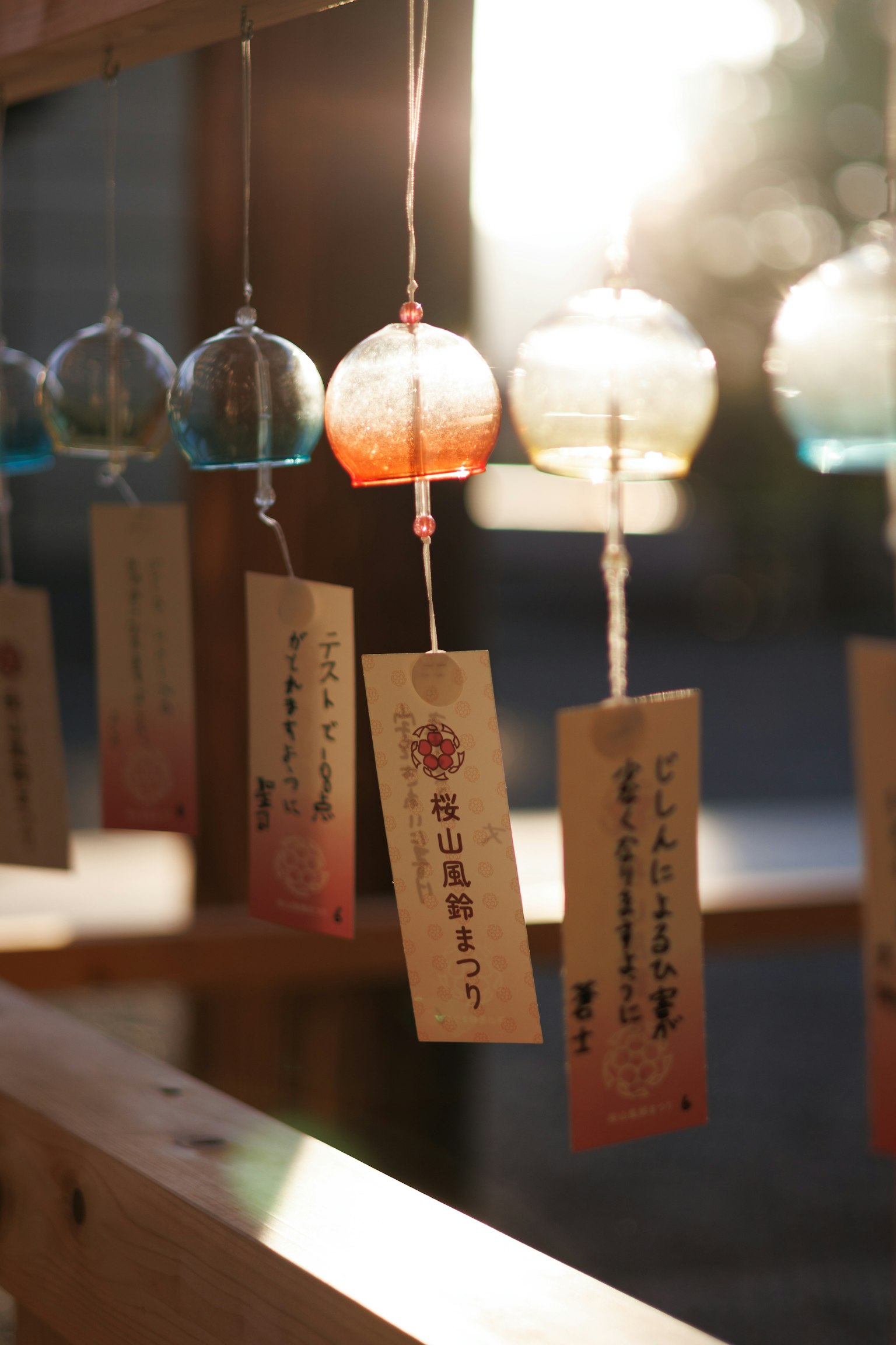 나무 구조물에 매달린 풍경 사진 투명한 풍경은 파란색과 주황색 색조가 있으며 각 풍경에는 단자가 부착되어 있음