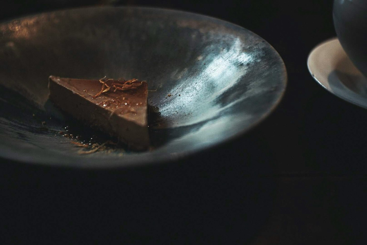 Una fetta di torta al cioccolato su un piatto scuro ed elegante con una tazza vicina