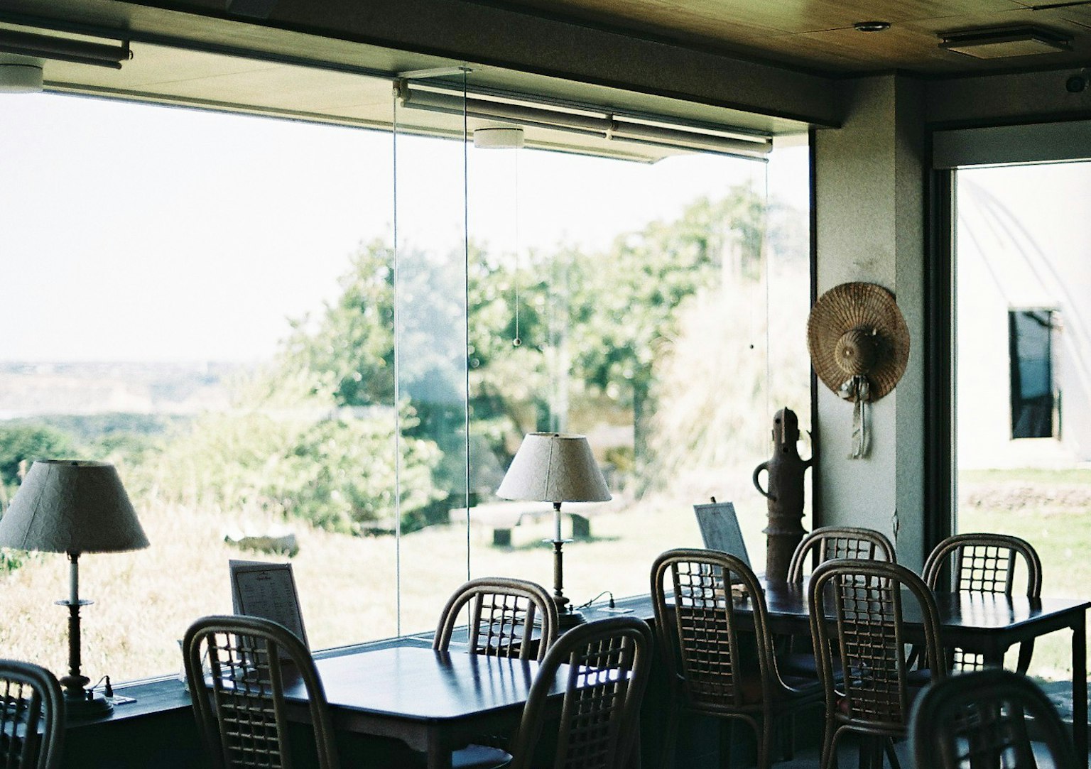 Interno di un caffè con grandi finestre luminose che mostrano tavoli e sedie con vista sulla vegetazione