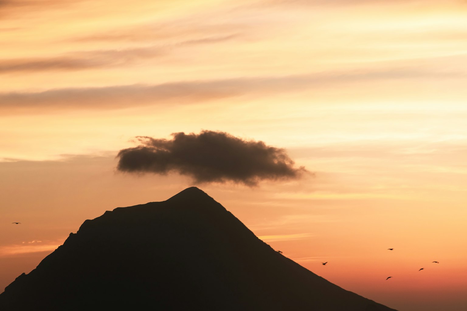Silhouette of a mountain with a cloud against a sunset sky