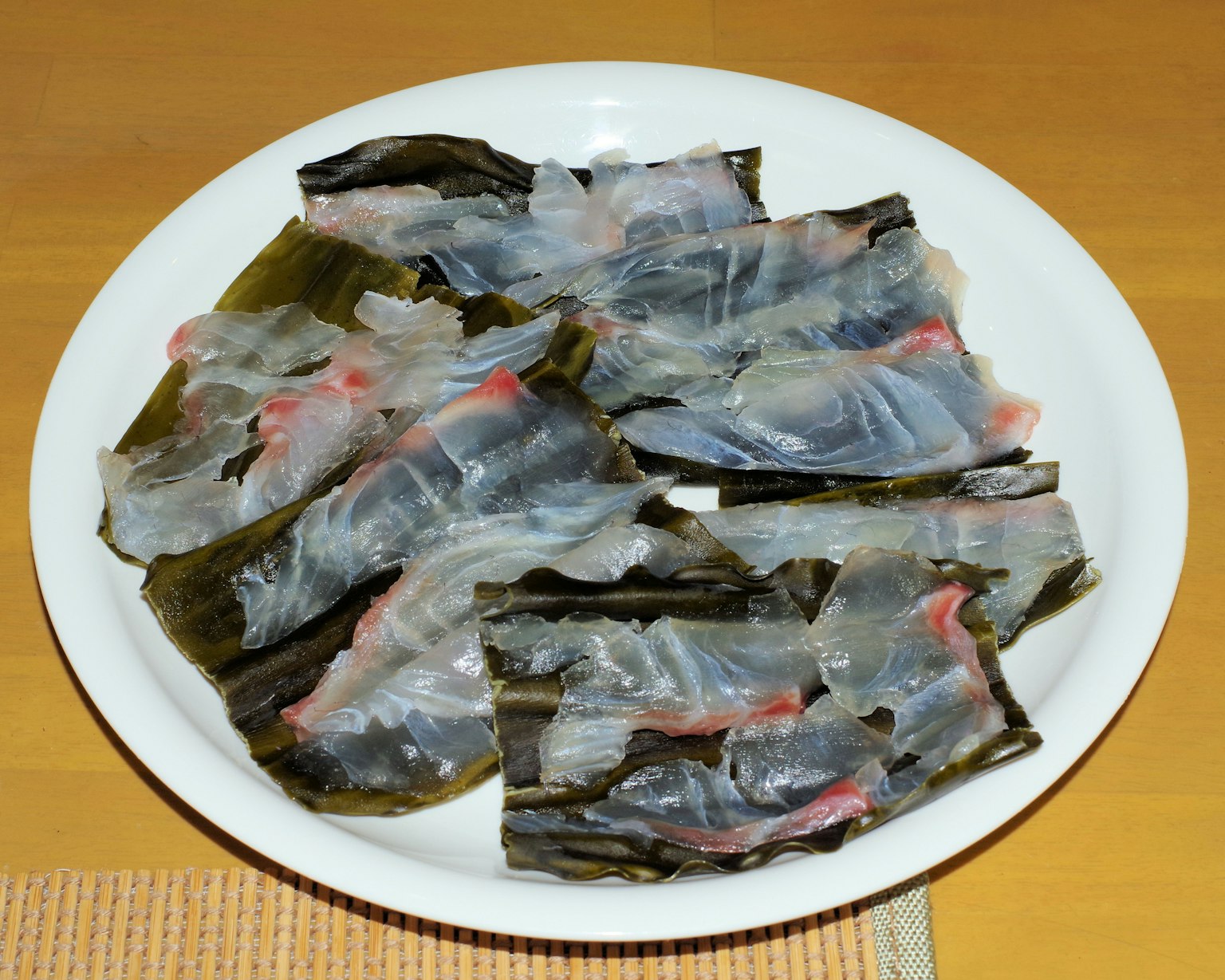 Piring berisi sashimi ikan transparan dengan rumput laut