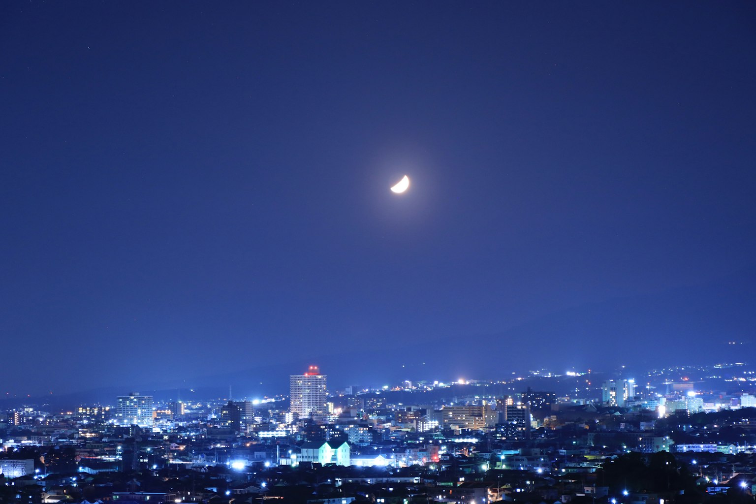 Langit malam dengan bulan sabit di atas cakrawala kota yang berkilau