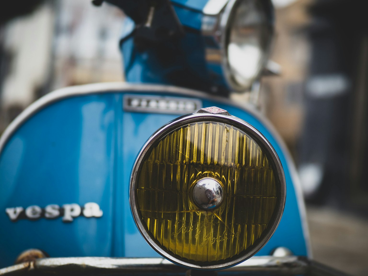 Close-up of a blue Vespa scooter's headlight and front section