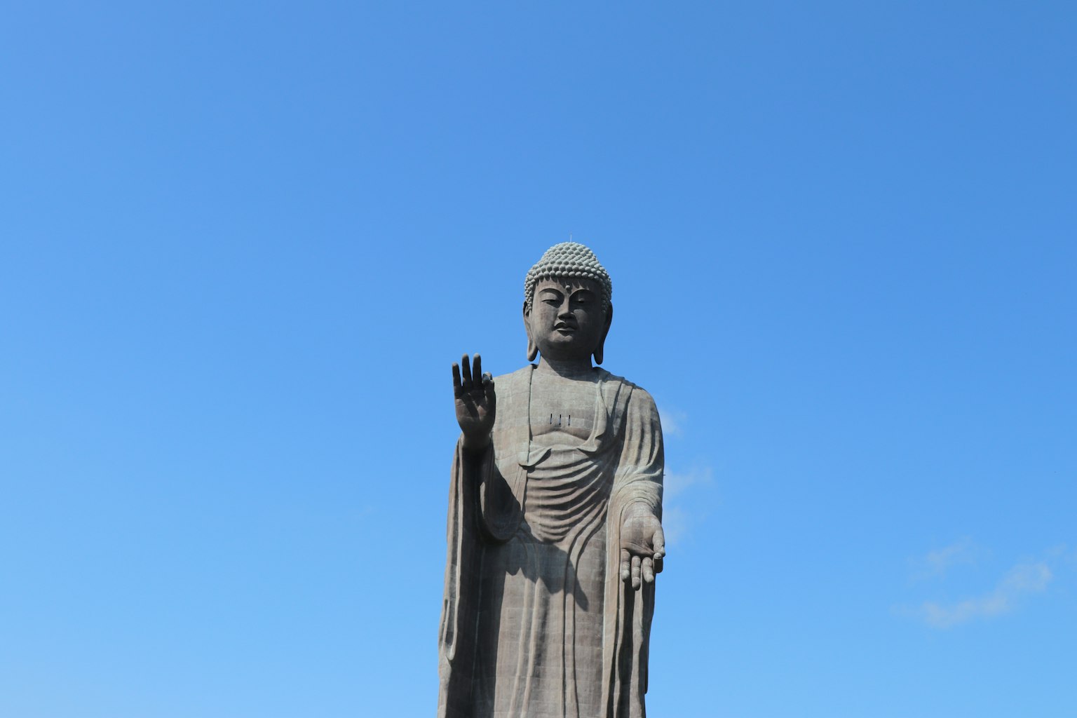 Grande statua del Buddha con la mano alzata contro un cielo blu chiaro