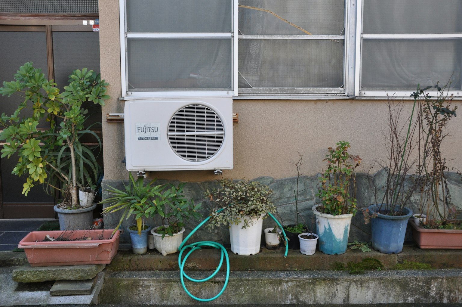 Potted plants arranged next to an air conditioning unit on a wall