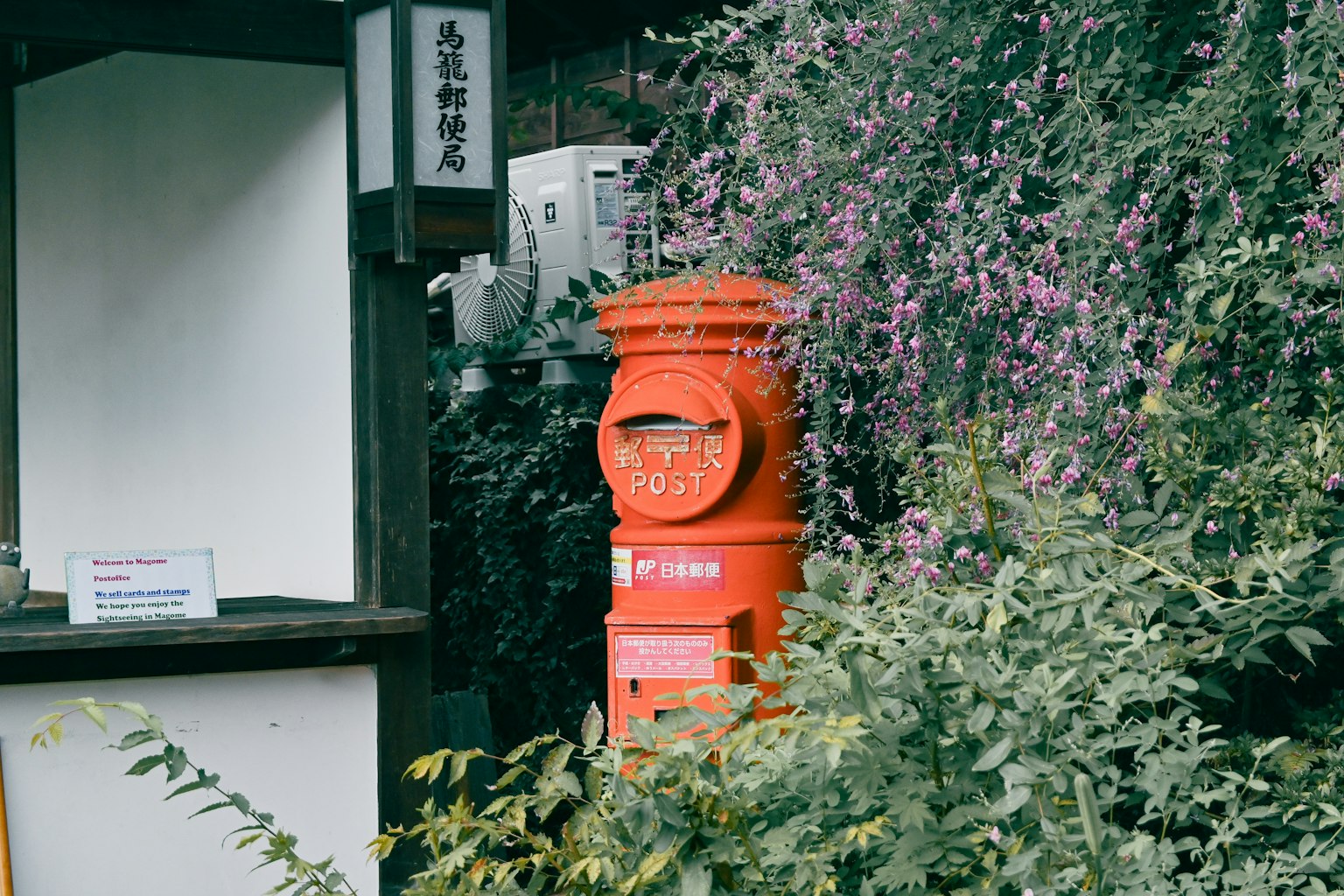 Boîte aux lettres rouge entourée de plantes vertes et d'un kiosque blanc