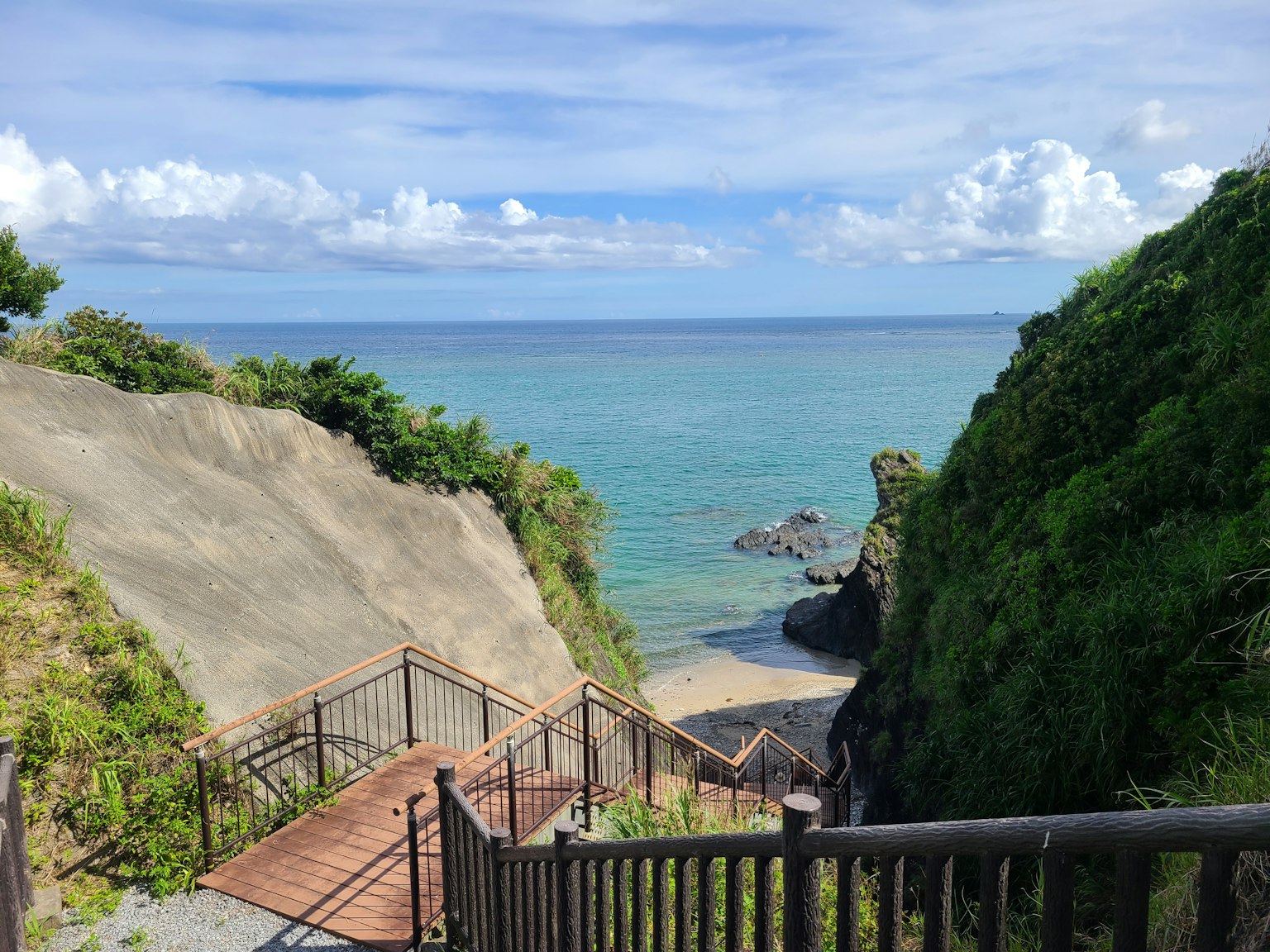 通往海滩的台阶景观，周围环绕着绿色山丘和蓝色海洋