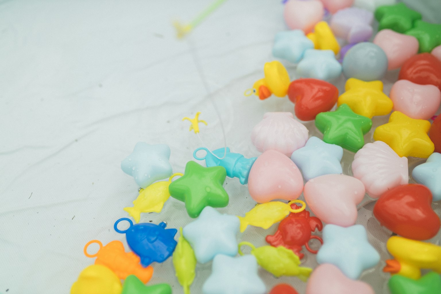 Perlas de plástico coloridas en formas de estrella, corazón y pez esparcidas sobre una superficie de agua