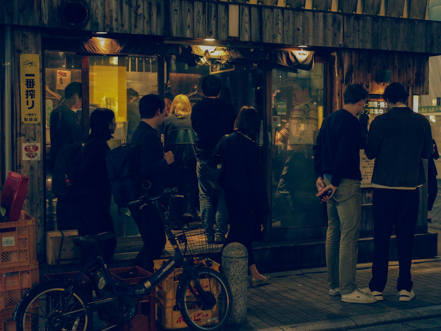 Busy restaurant exterior at night with a queue of people
