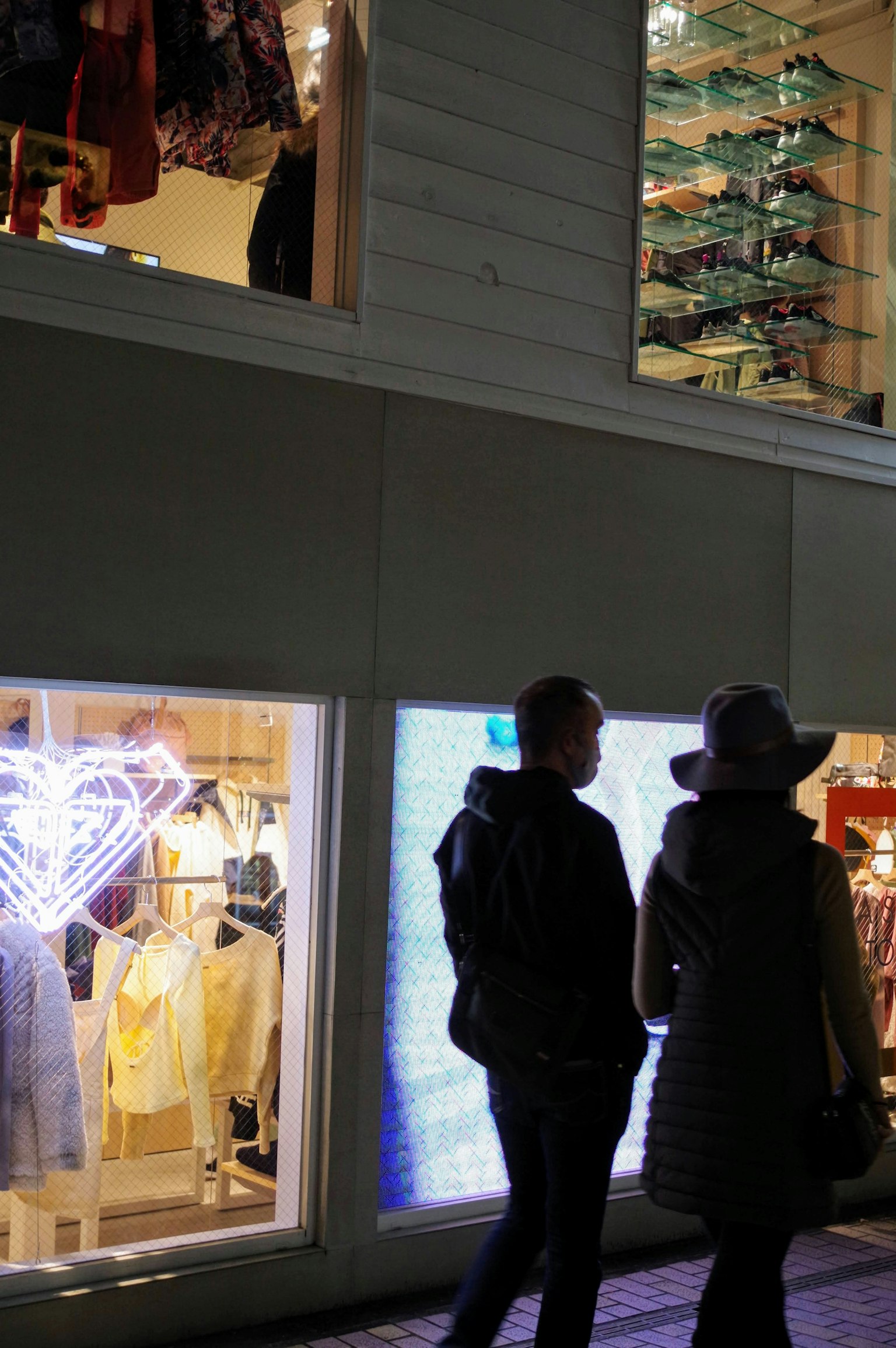 Two people standing in front of a brightly lit shop window at night