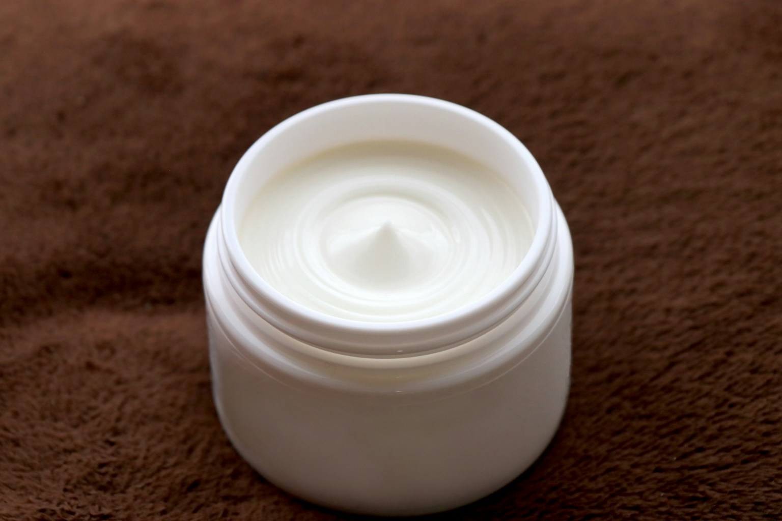 Una crema bianca in un barattolo su uno sfondo di tessuto marrone