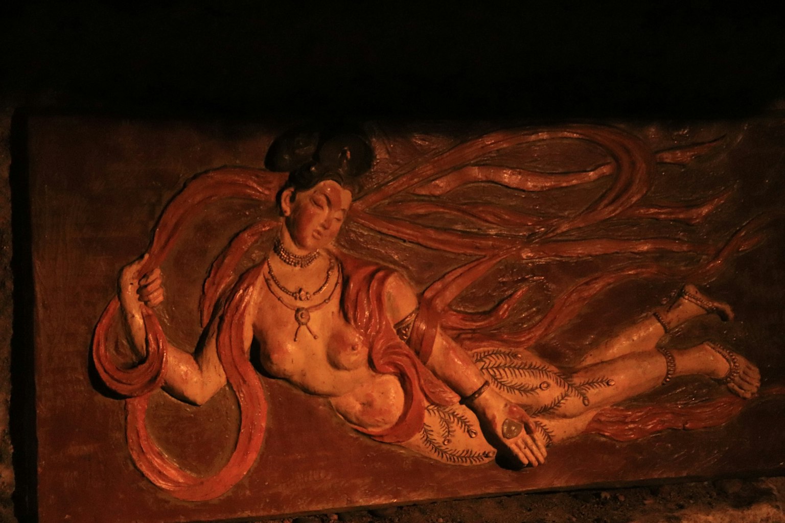 Escultura antigua de una mujer con cabello rojo reclinada en una pose misteriosa