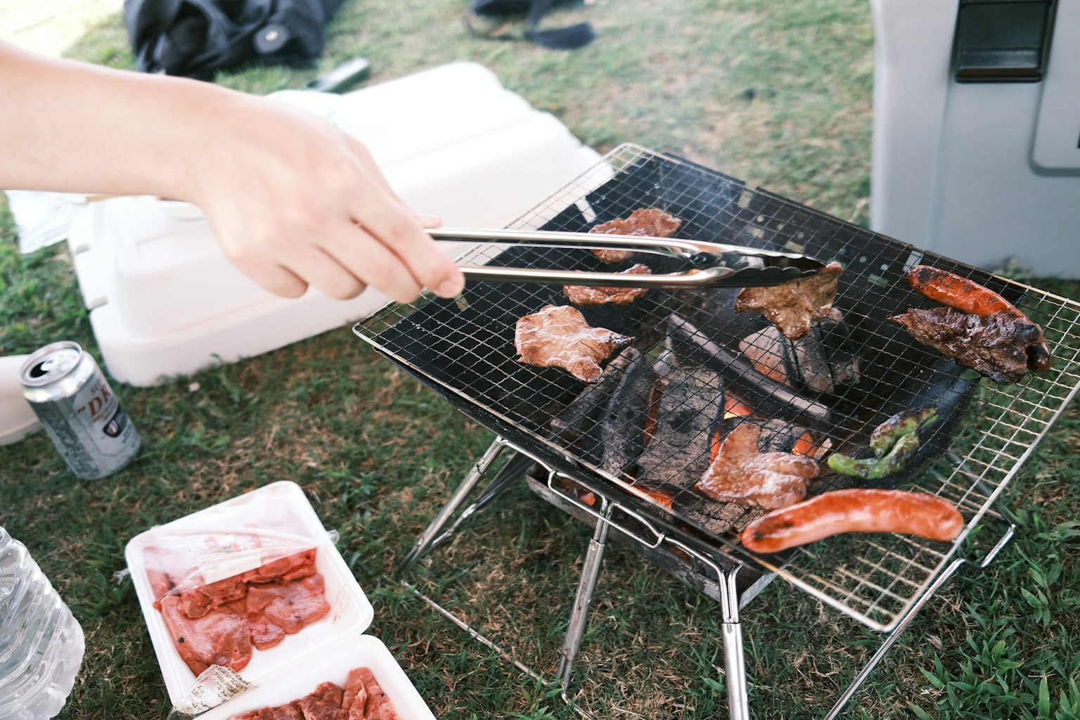 A hand using tongs to flip meat on a barbecue grill