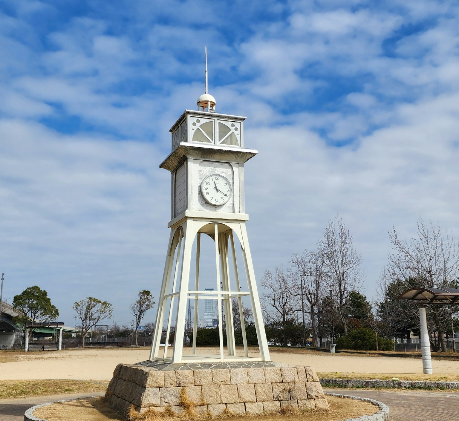 Une horloge blanche se tenant dans un parc sous un ciel bleu