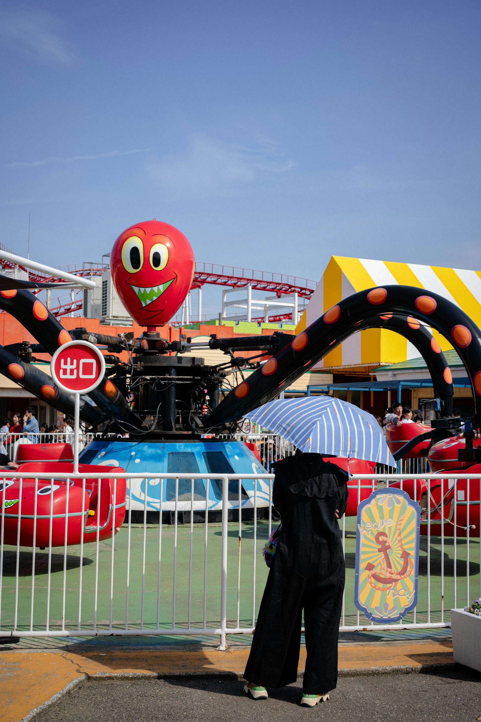 カラフルなタコの遊具と傘を持つ人がいる遊園地の風景
