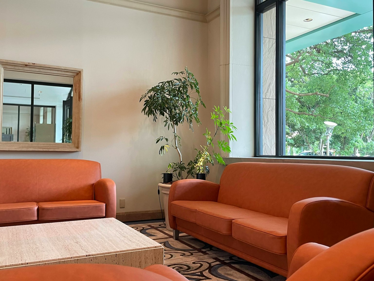Góc phòng khách ấm cúng với ghế sofa màu cam sáng và bàn cà phê Cảnh xanh nhìn thấy qua cửa sổ lớn Gương treo tường thêm phần thanh lịch