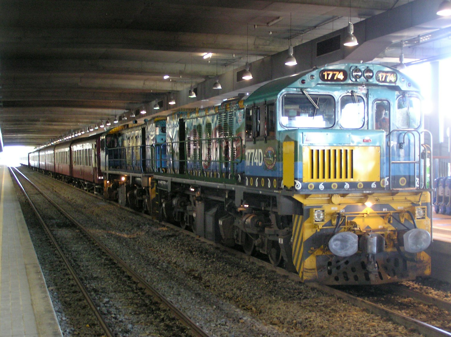 Locomotive bleue et jaune avec des voitures de passagers à une station