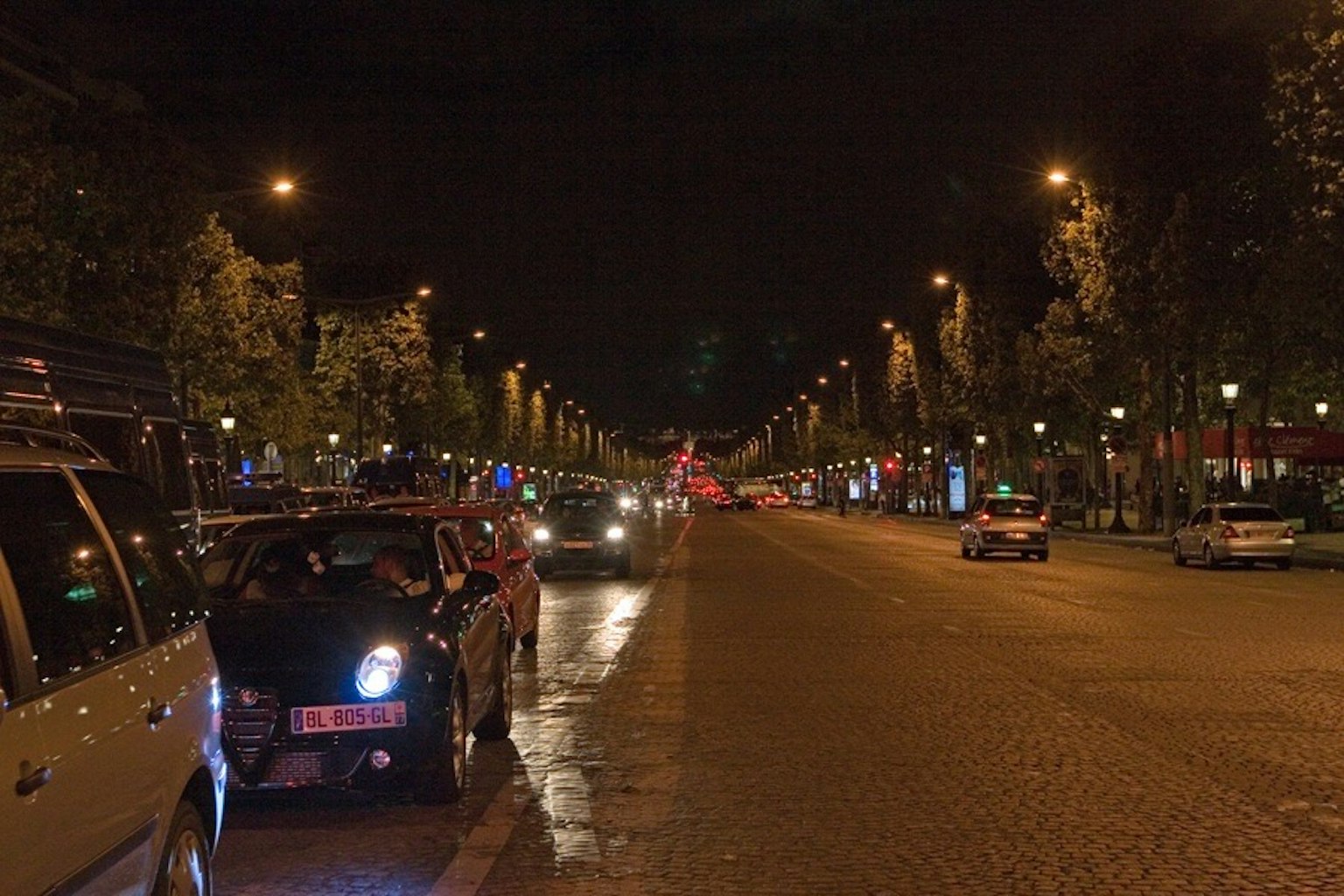 Pemandangan malam Champs-Élysées dengan mobil parkir dan lampu jalan