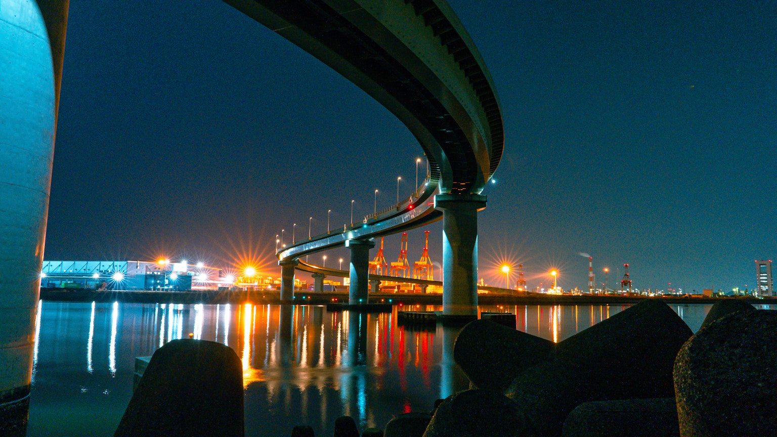 ทิวทัศน์เมืองยามค่ำคืนที่มีสะพานสูงเหนือผิวน้ำและหิน