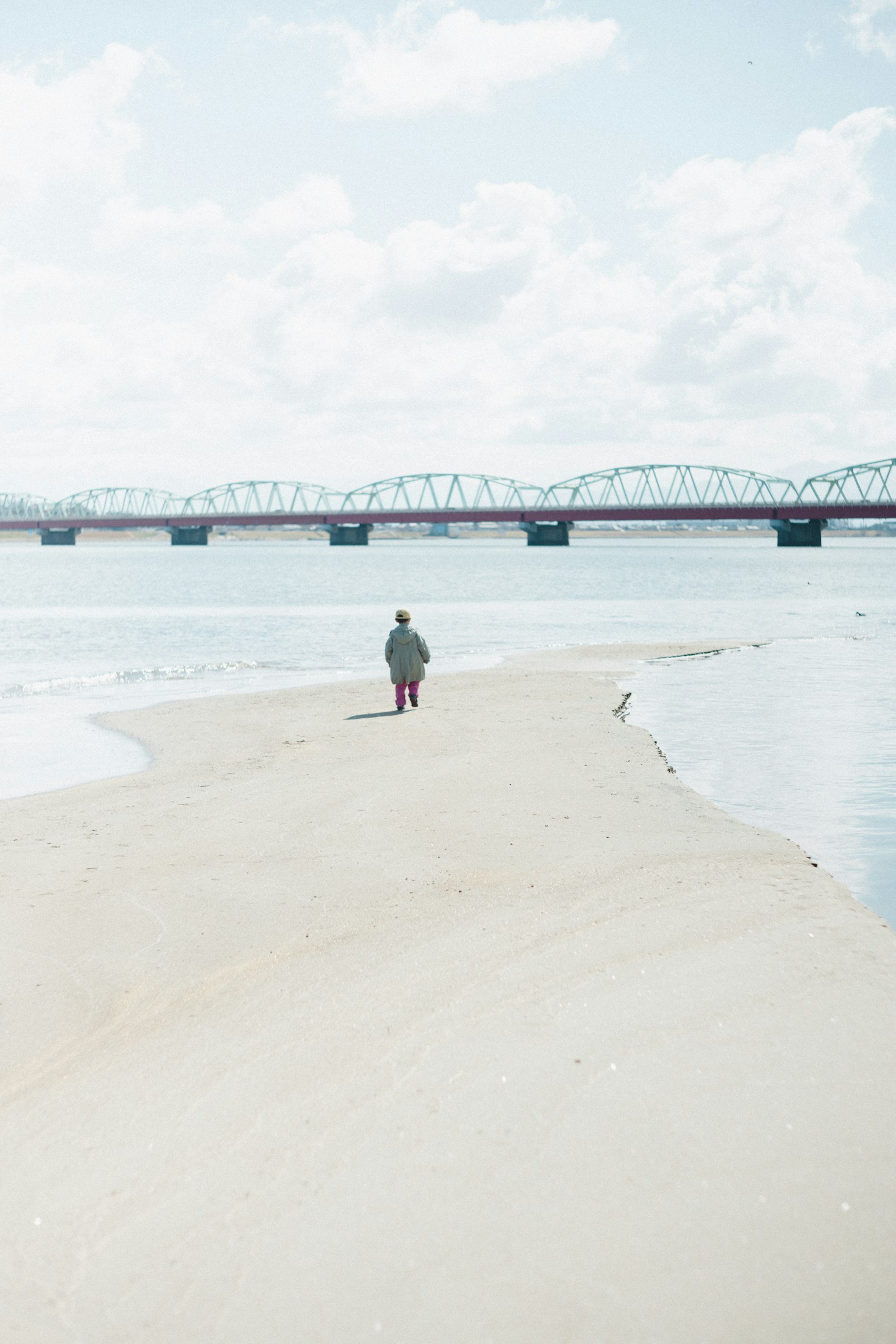 Una persona caminando por la orilla tranquila de un río con un puente al fondo