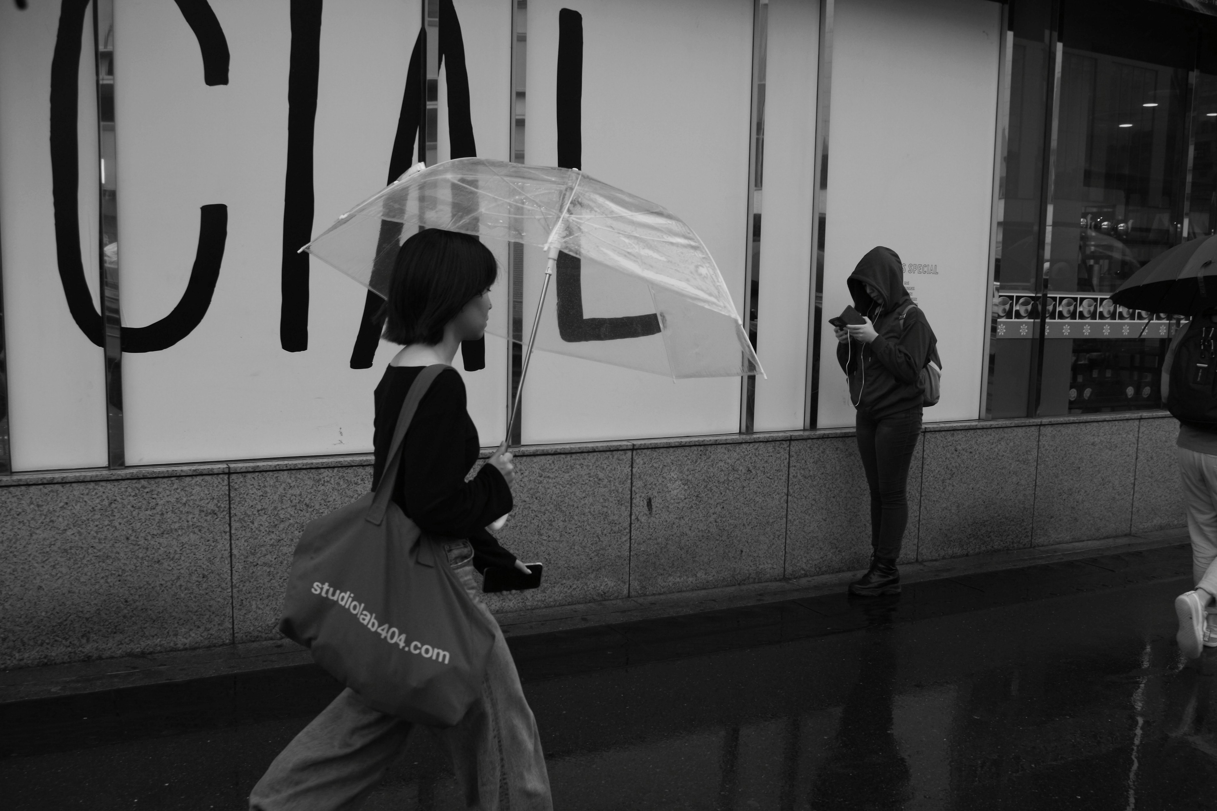 雨の路上で傘をさす人と買い物袋のある街角
