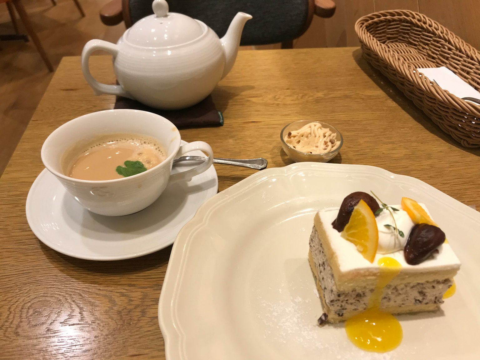 白色茶壶和一杯茶，咖啡桌上的水果装饰蛋糕一片