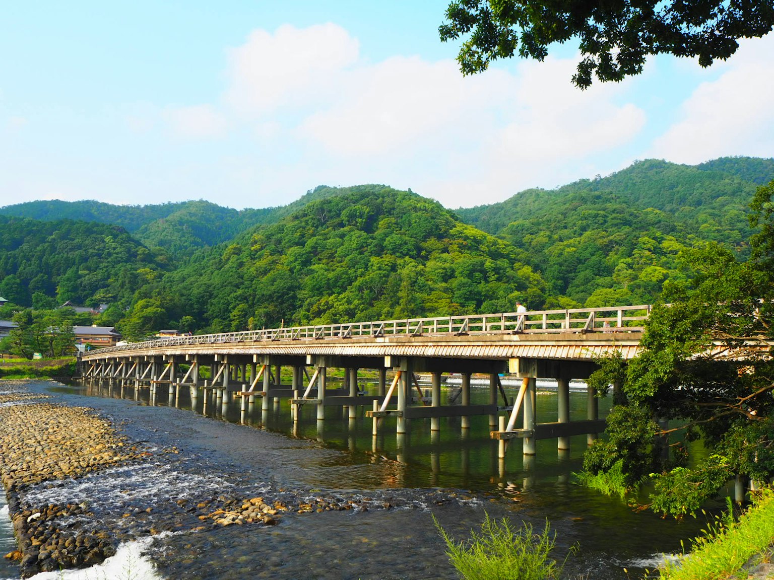 Pont en bois traversant une rivière avec des montagnes vertes en arrière-plan