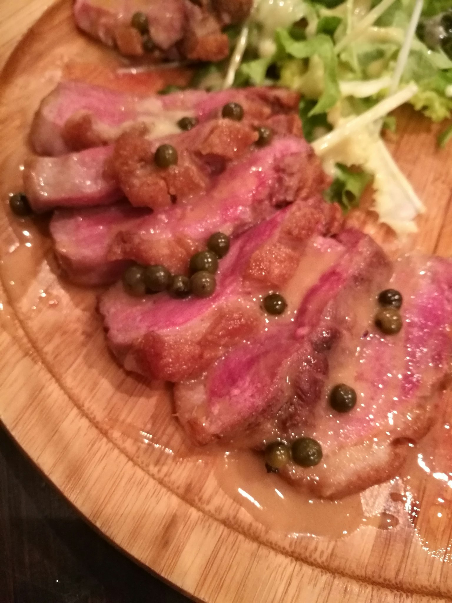 Sliced meat dish with green vegetable garnish and sauce