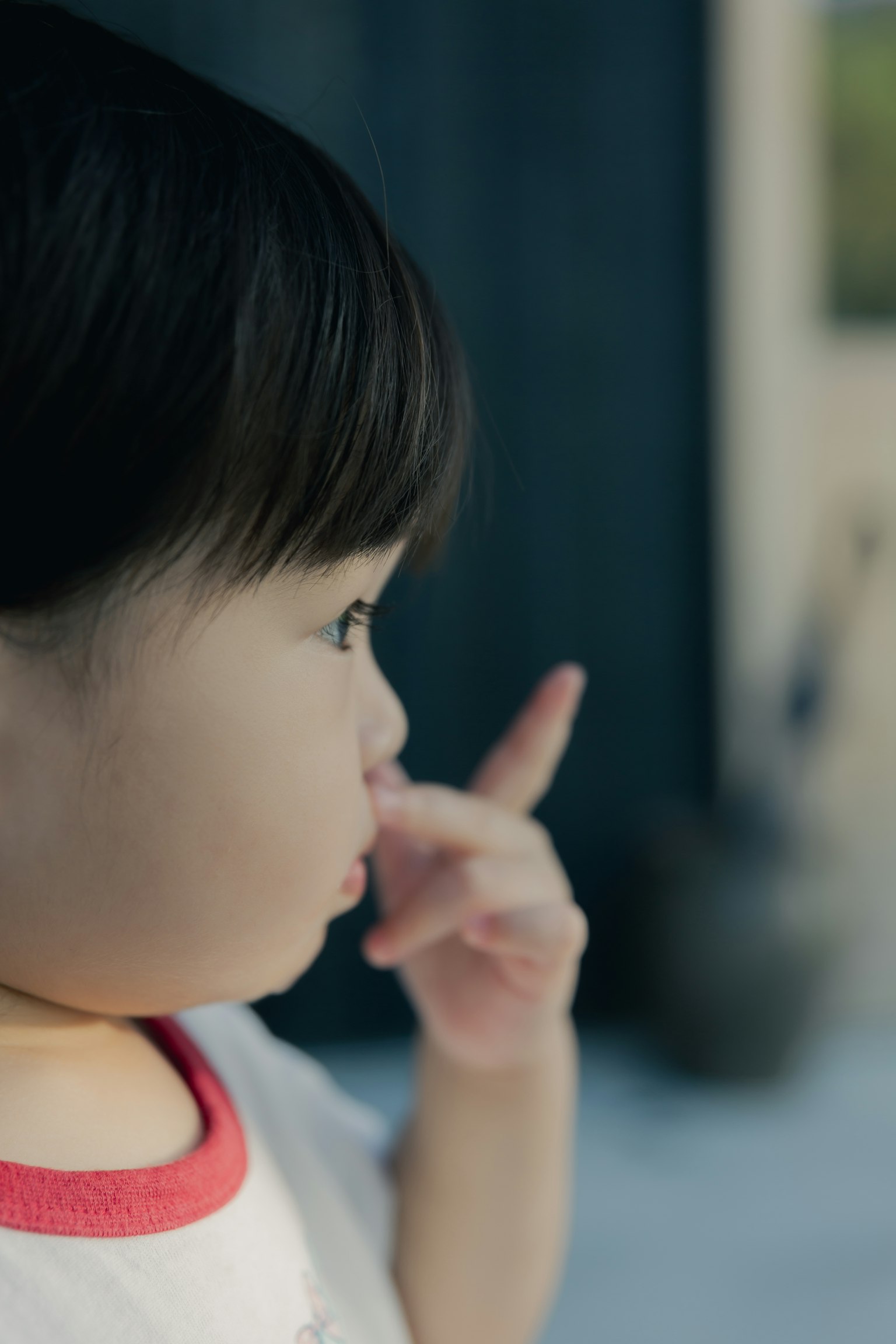 Un tout-petit en t-shirt à bord rouge lève un doigt de profil