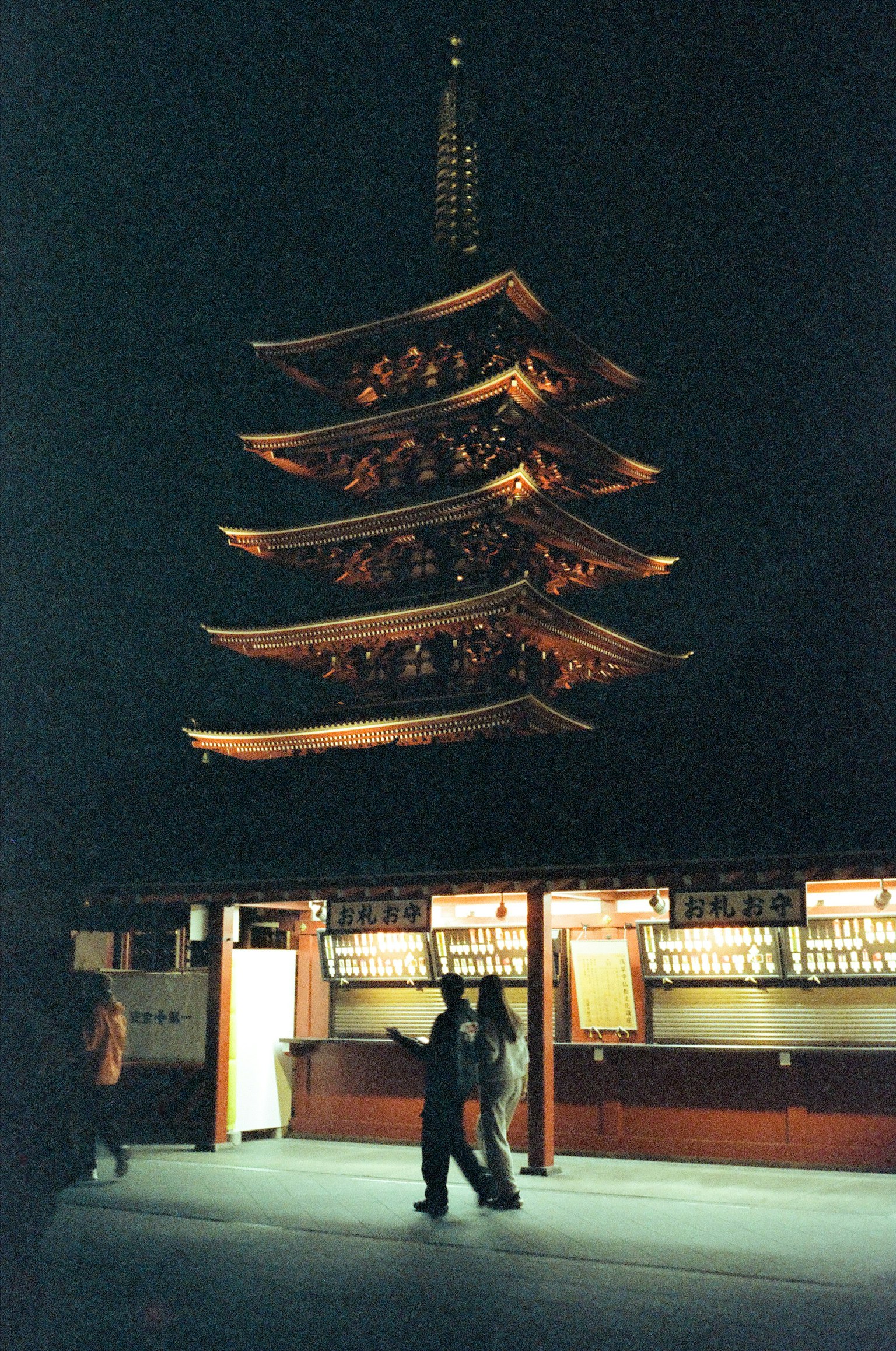 Illuminated pagoda at night with silhouettes of people