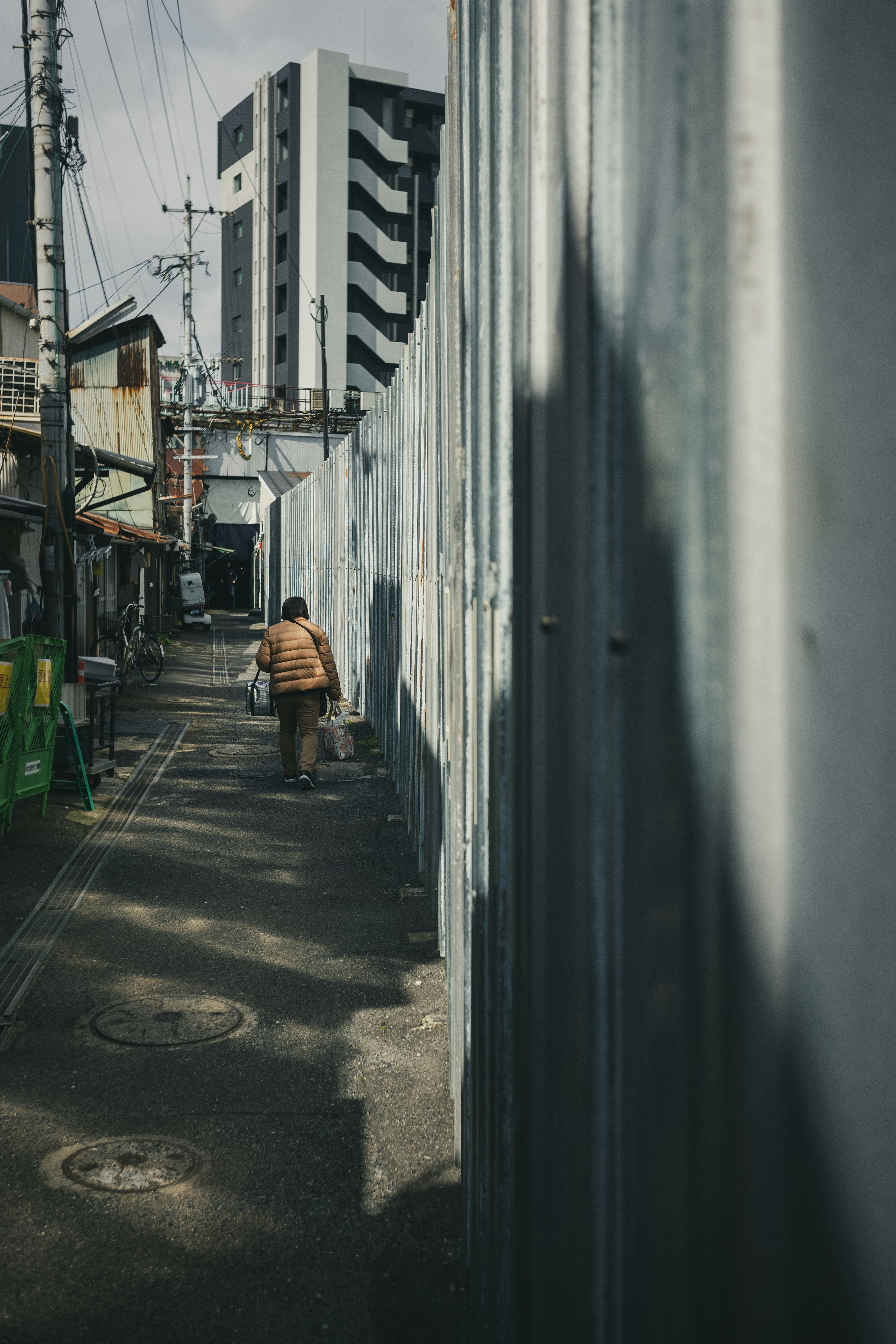 Una persona caminando junto a un muro en un callejón, con rascacielos al fondo