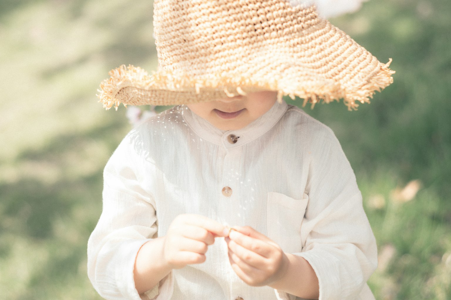 Child wearing a straw hat examining a small object on the grass