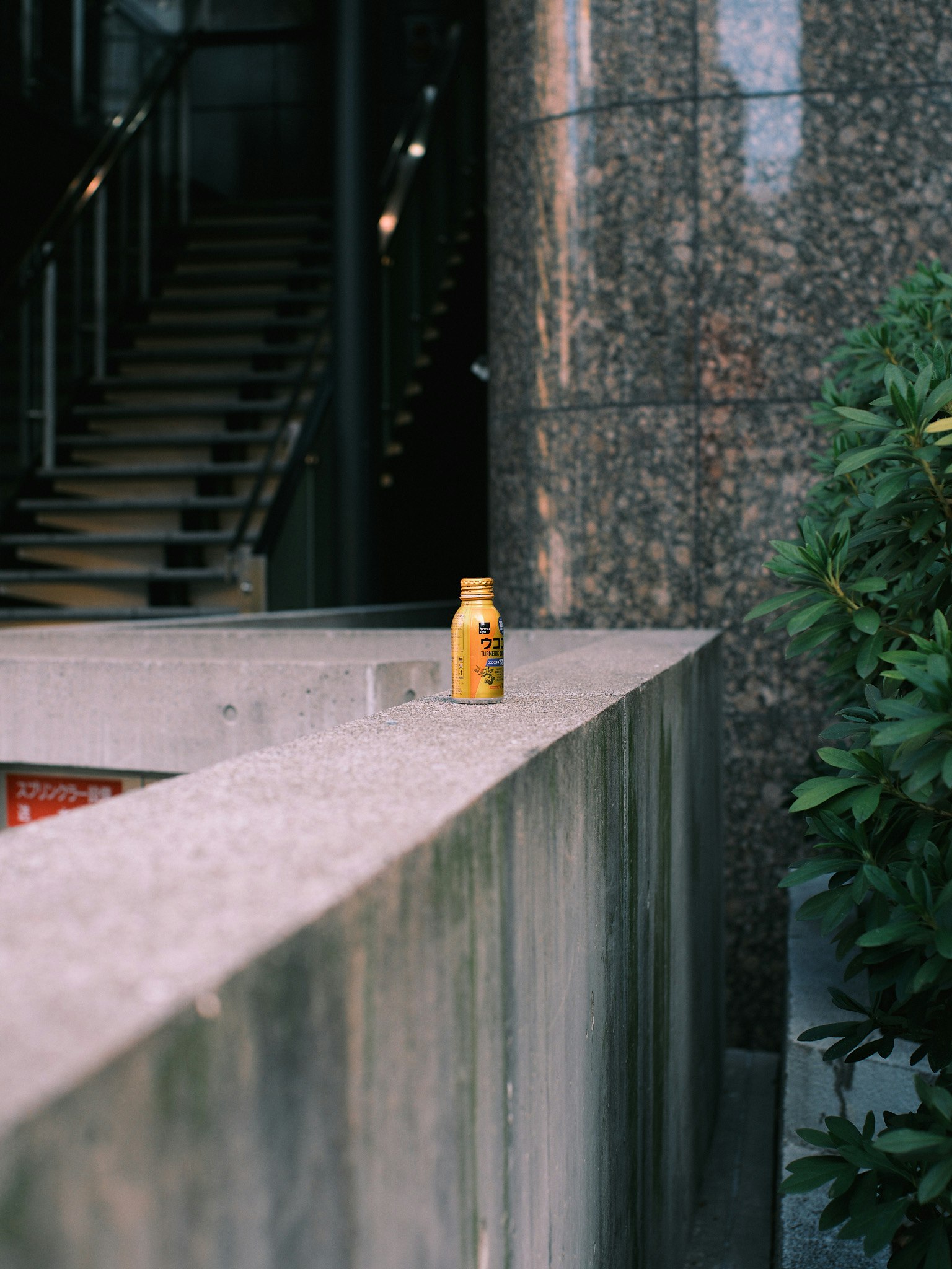 Yellow beverage bottle placed near stairs on a concrete ledge