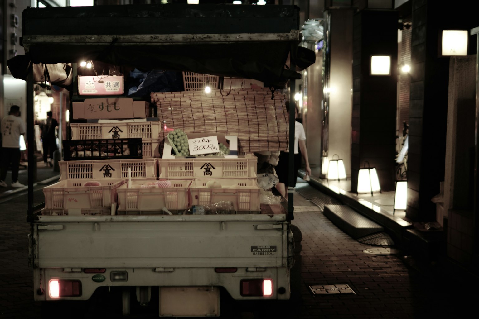 A truck loaded with boxes parked in a narrow alley at night