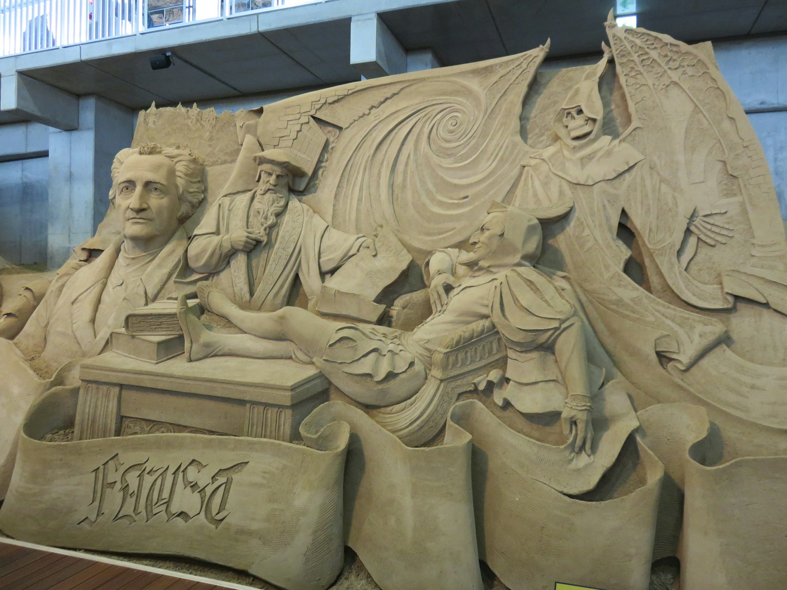 Sandskulptur mit mehreren Figuren und erzählerischen Elementen