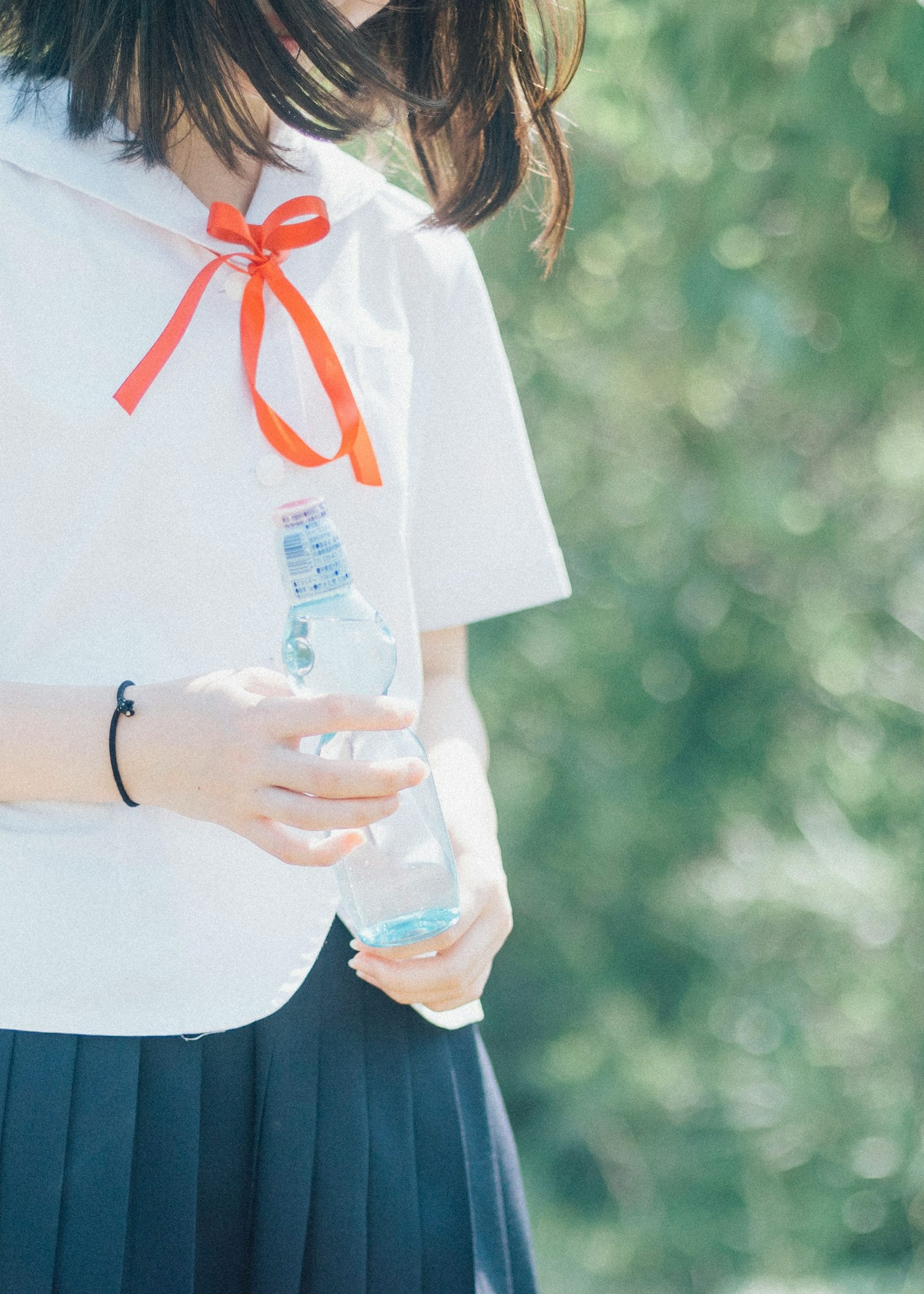 Un estudiante con una camisa blanca y un lazo rojo sosteniendo una botella de agua
