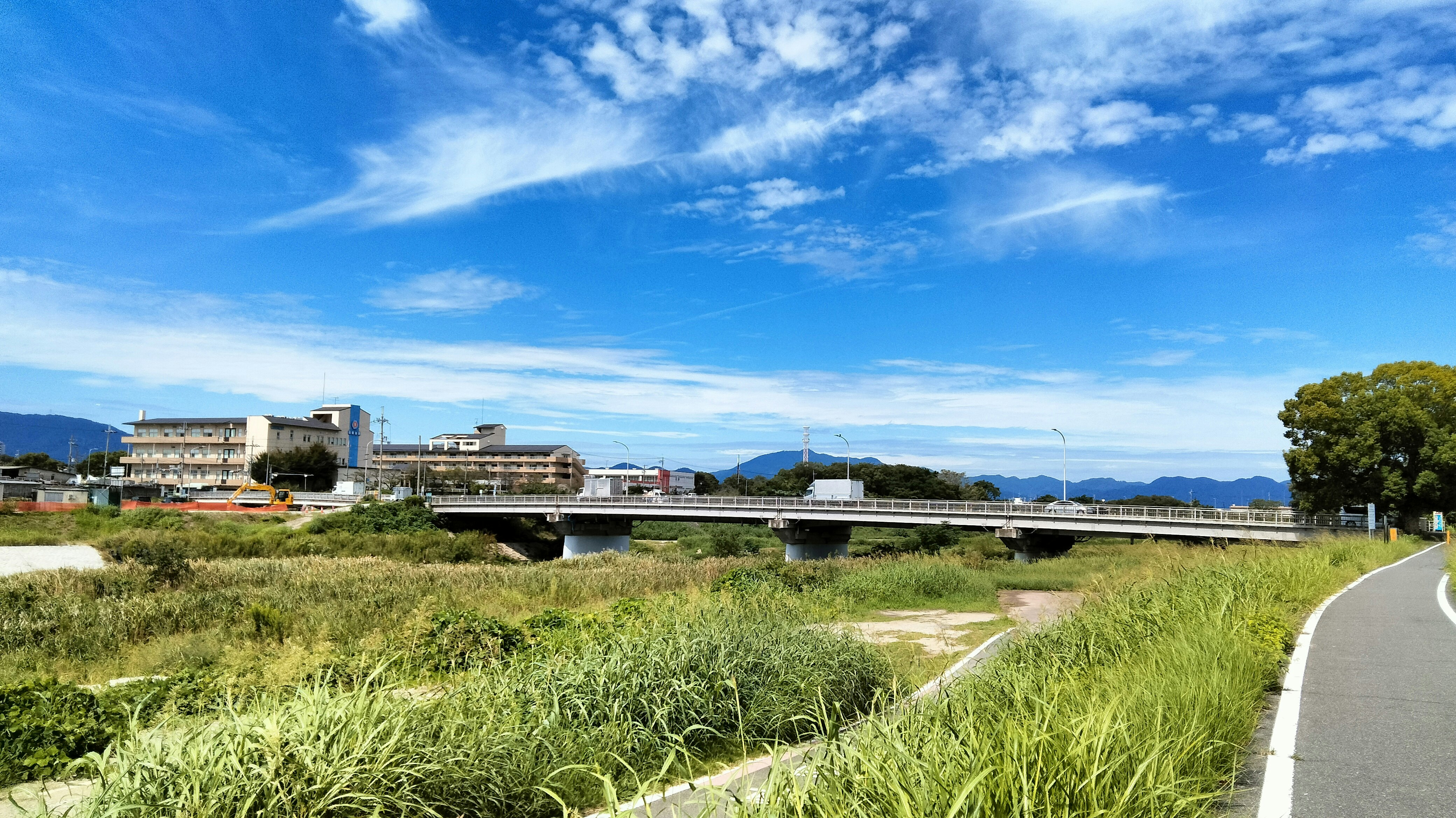 川沿いの草地と遠くの山並み、青空の風景